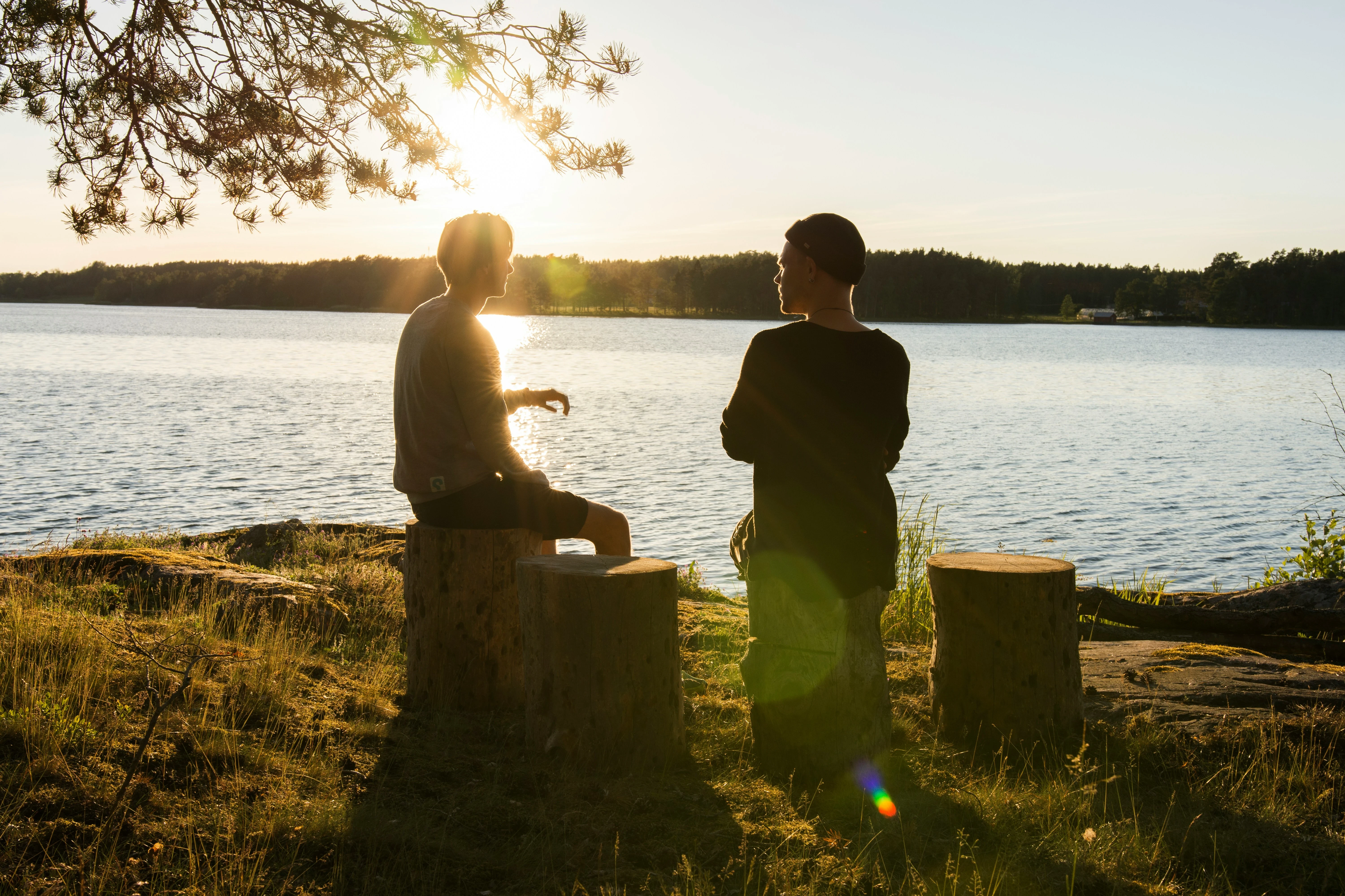 Zwei junge Männer sitzen bei Sonnenuntergang am See und reden